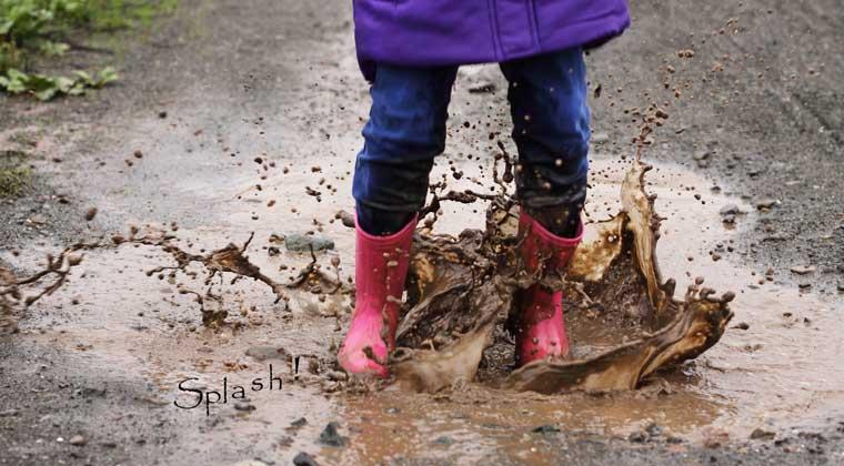 girl with rain boots jumping in puddle