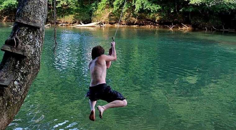 boy at lake on rope swing